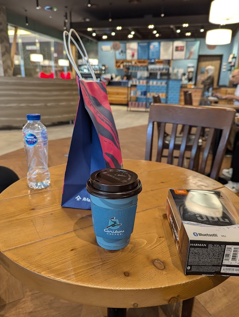 A table at Caribou Coffee with a coffee cup, water bottle, and a JBL speaker box.