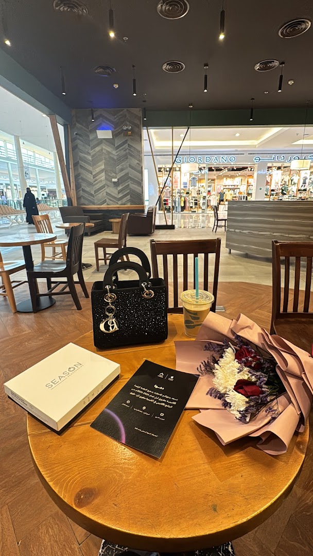 A table at Caribou Coffee with a handbag, drink, gift box, and flowers.