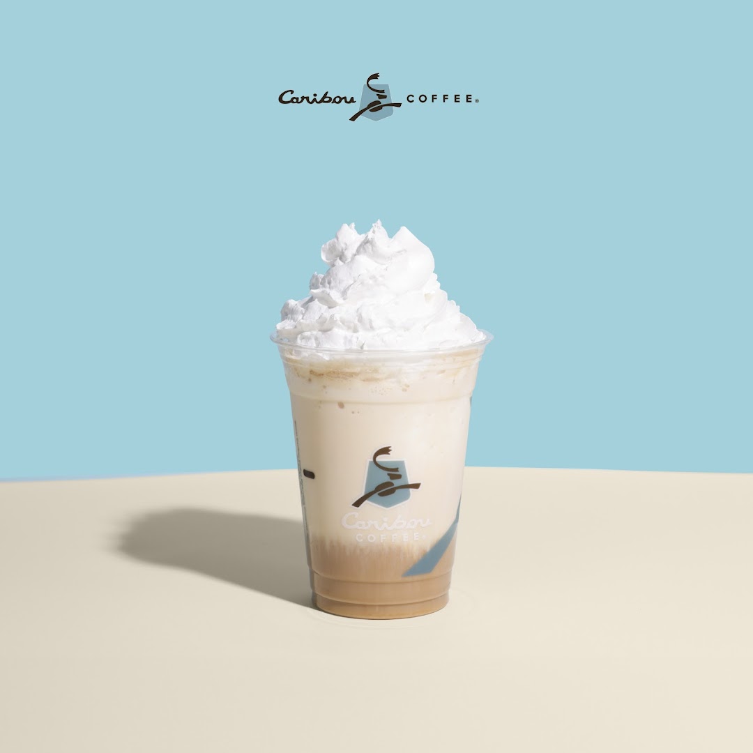 A Caribou Coffee beverage with whipped cream in a clear plastic cup.
