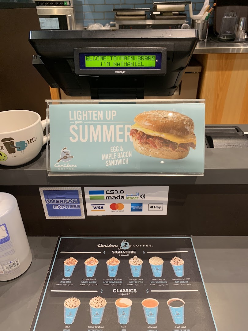 A Caribou Coffee counter displaying a summer sandwich promotion and a menu of drinks.