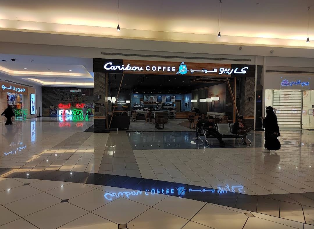 The exterior of a Caribou Coffee shop in a mall, with seating areas inside and outside.