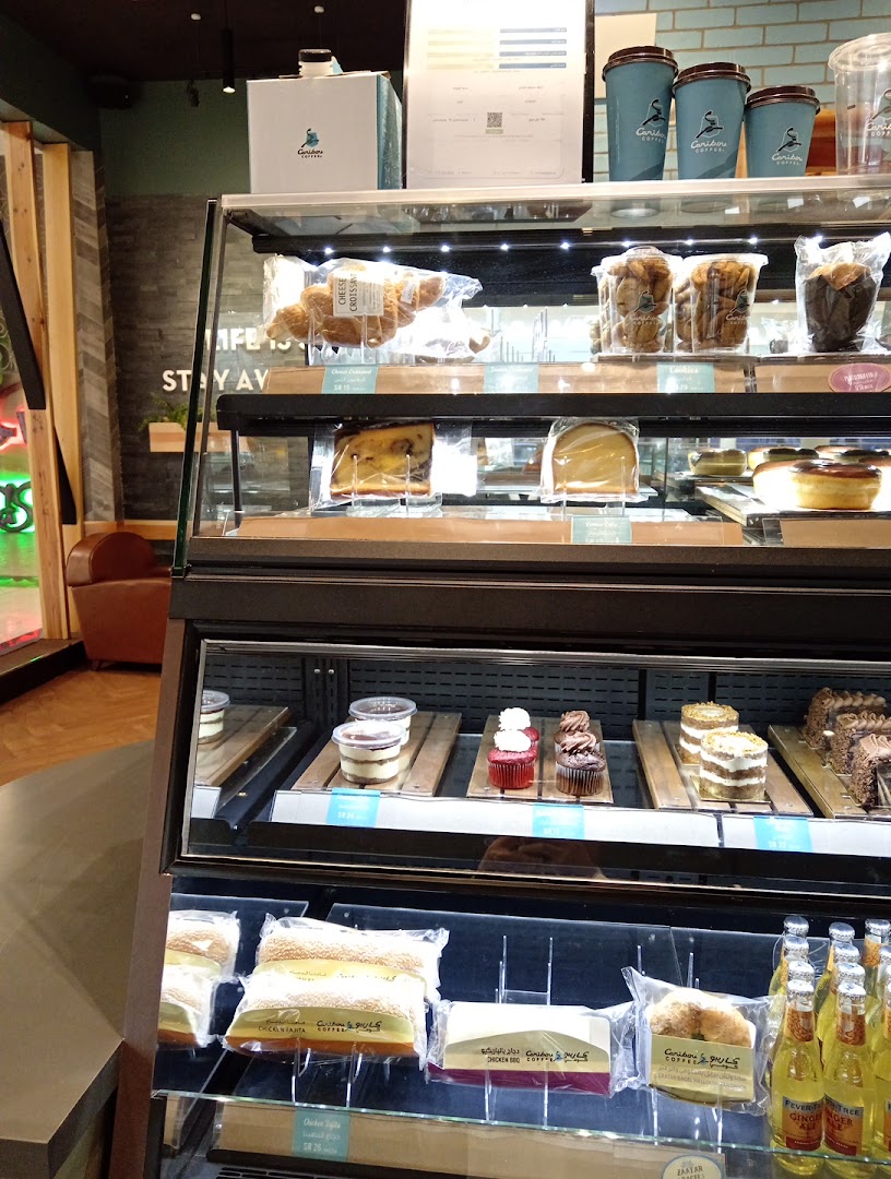 A display case filled with various pastries, cakes, and bottled drinks at Caribou Coffee.