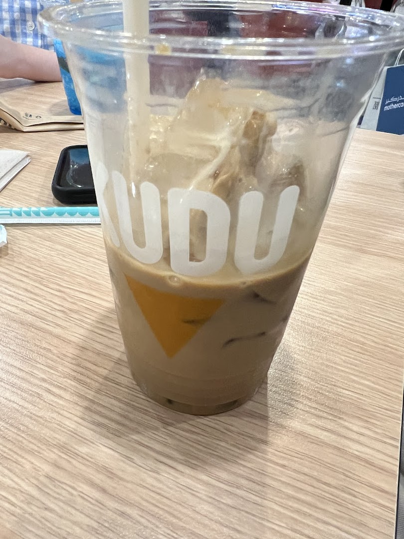 A close-up of an iced coffee drink in a clear plastic cup with the Kudu logo.