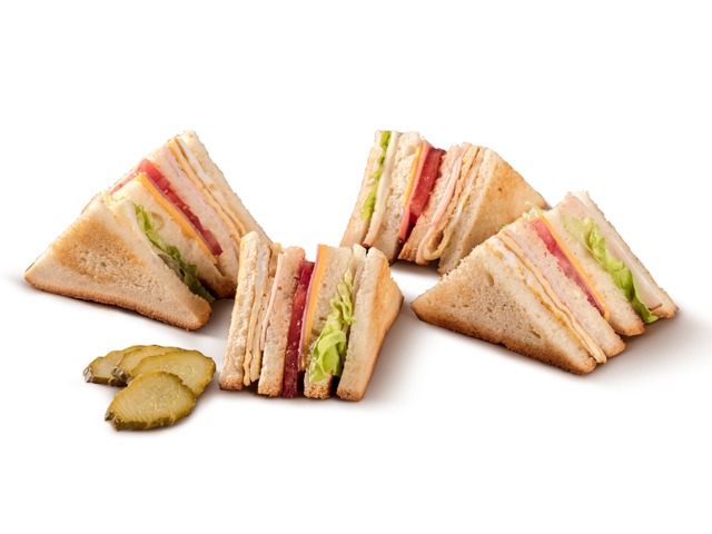 Several delicious club sandwiches and pickle slices arranged on a white background.