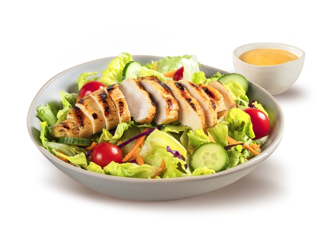 A delicious grilled chicken salad with fresh lettuce, tomatoes, cucumbers, and a side of dressing.