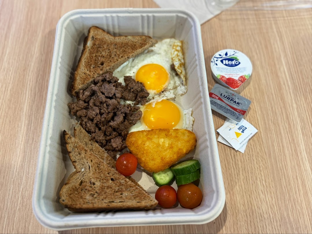 A hearty breakfast meal in a takeaway container with toast, eggs, minced meat, hash brown, and sides.