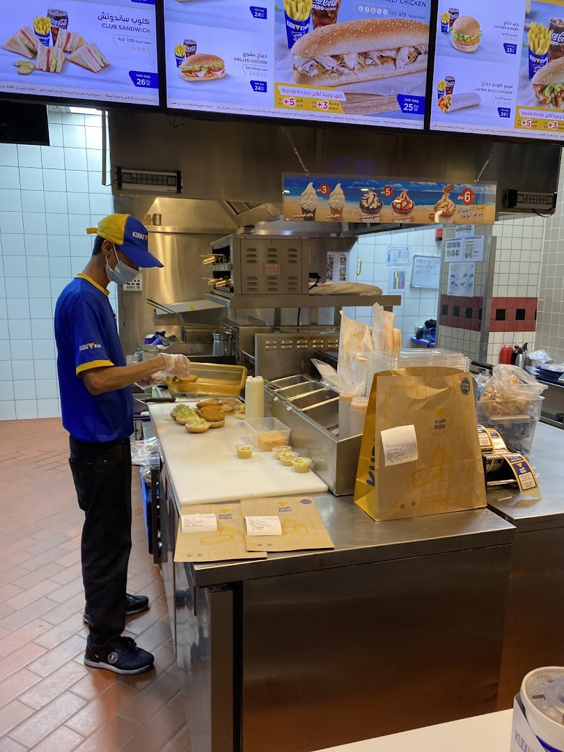 A worker prepares food behind a counter with digital menus displaying food items.
