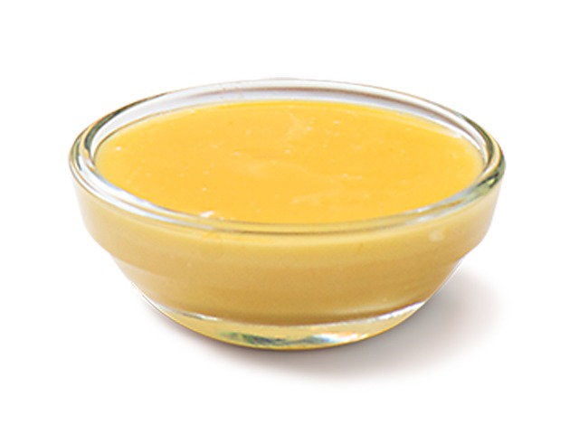 A close-up shot of a glass bowl filled with a creamy yellow sauce or dip.