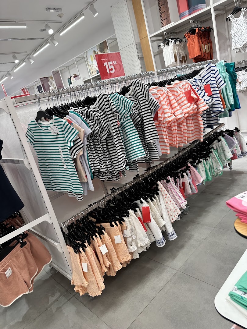 A retail store interior displaying rows of children's clothing on hangers, with a sale sign visible.