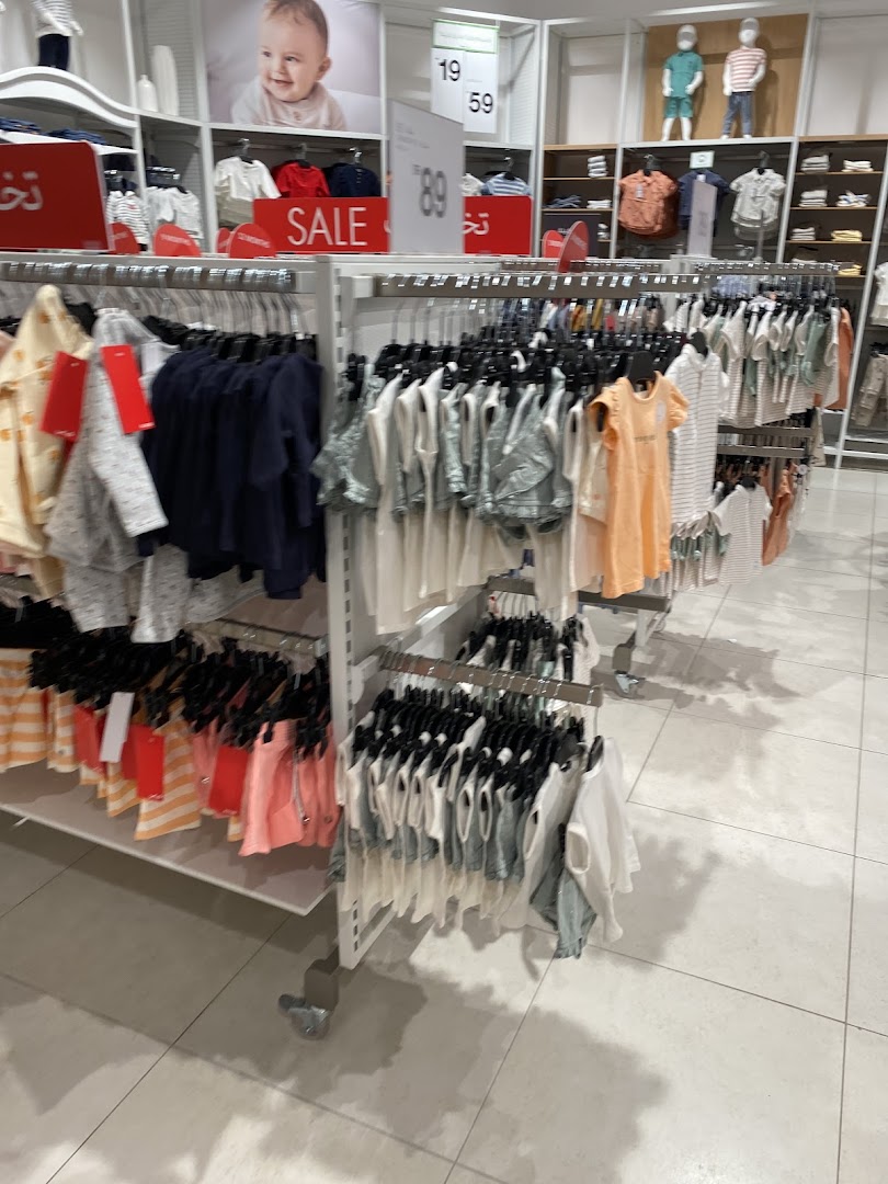 A brightly lit children's clothing store with racks of colorful apparel and sale signs.