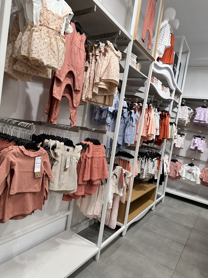 A well-organized display of children's clothing, featuring dresses, rompers, and outfits in various pastel colors.