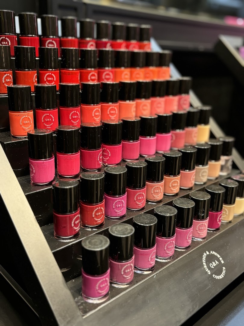 A display of colorful nail polish bottles from QA Cosmetics arranged on tiered shelves.