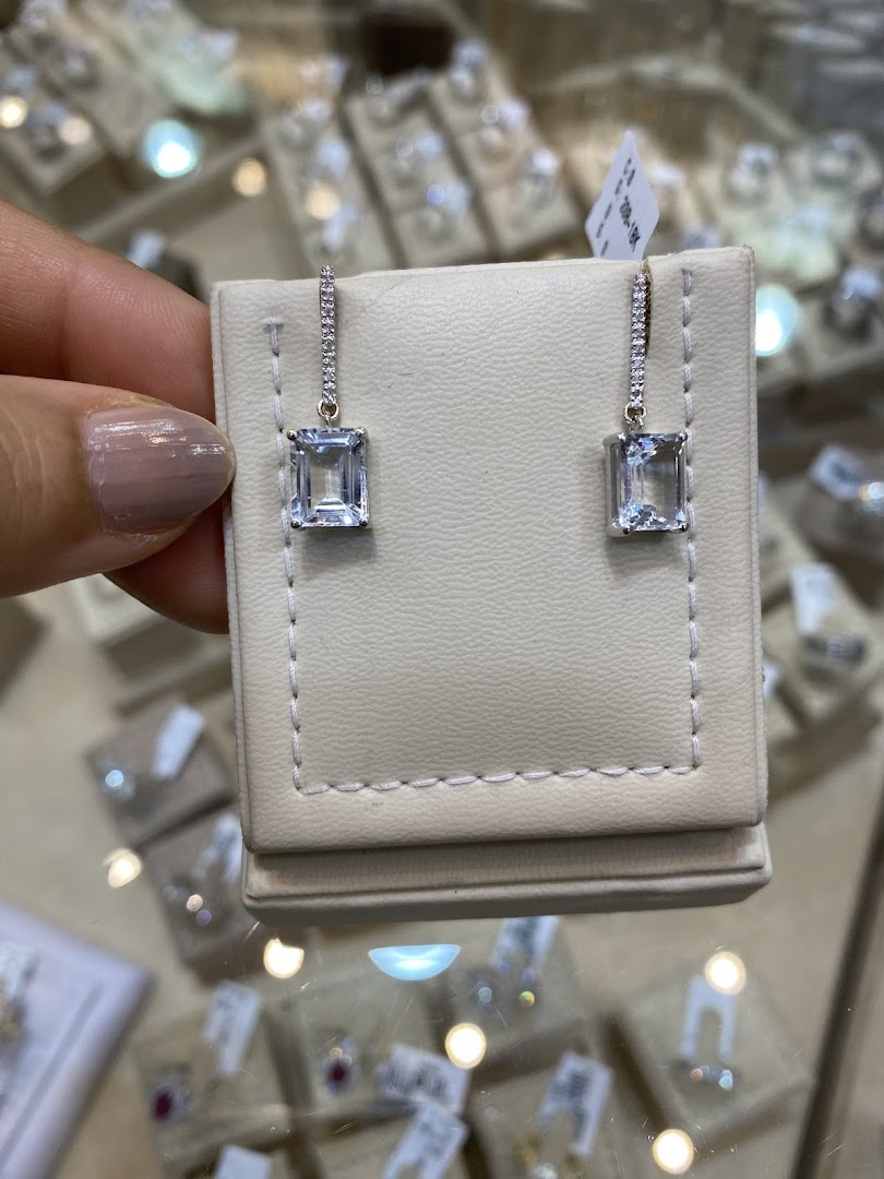A hand holds a pair of elegant diamond and aquamarine drop earrings.