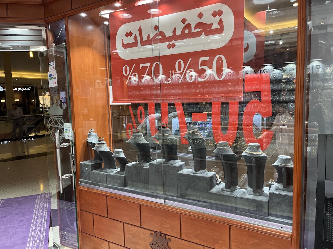 A jewelry shop window displays necklaces on stands with a large sale sign in Arabic.