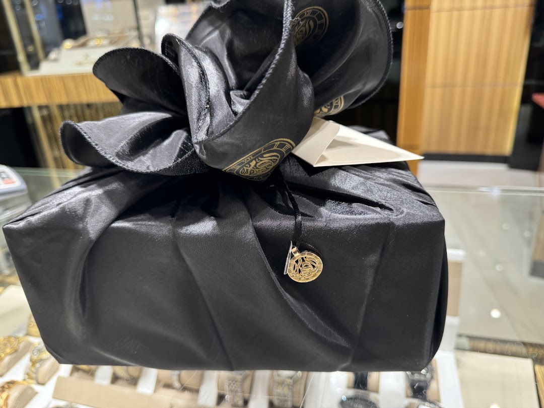 A beautifully wrapped black gift box with a golden charm and tag, presented in a retail setting.