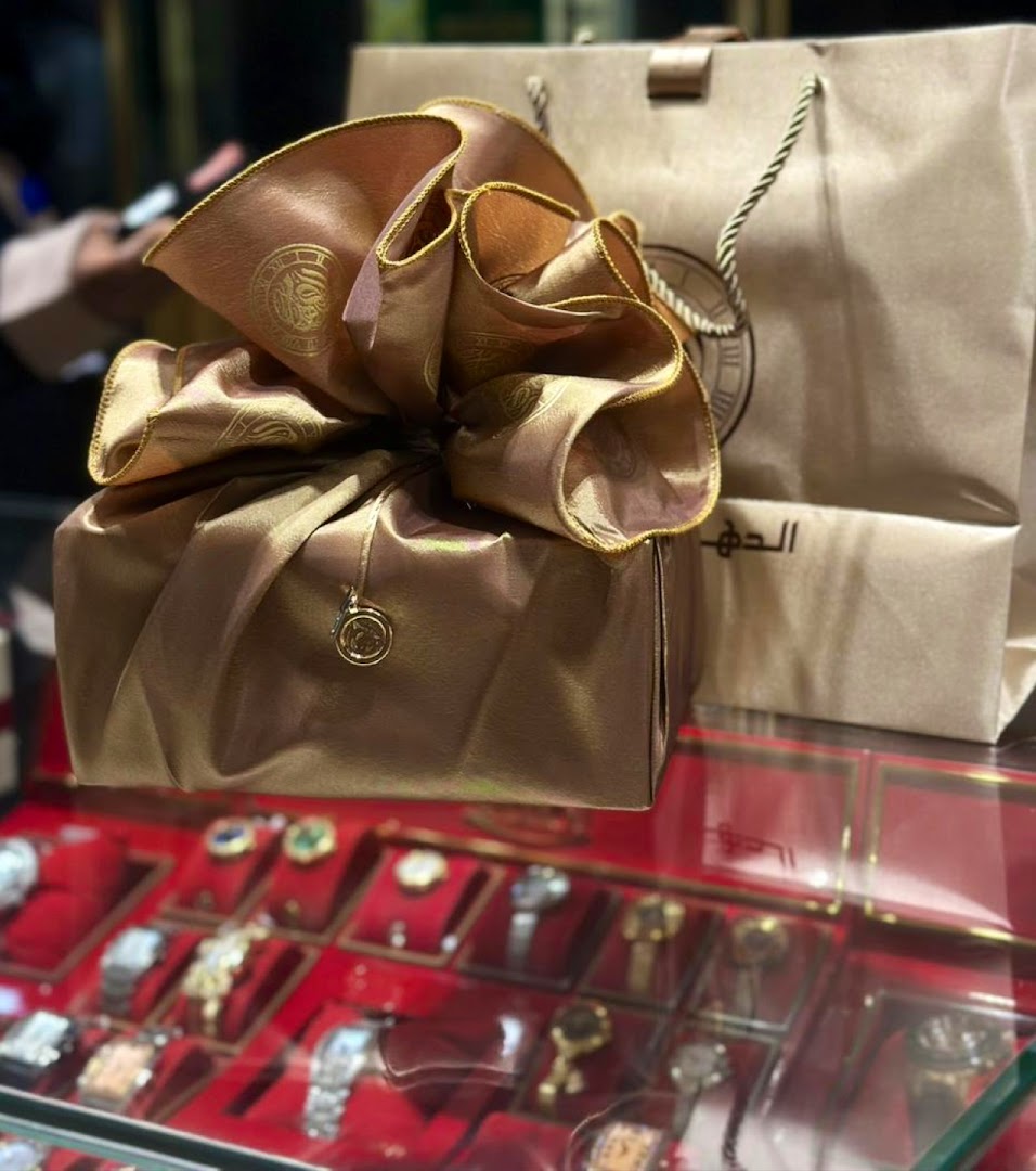 A beautifully wrapped gift with a large bow sits in front of shopping bags from ALDAHAM.