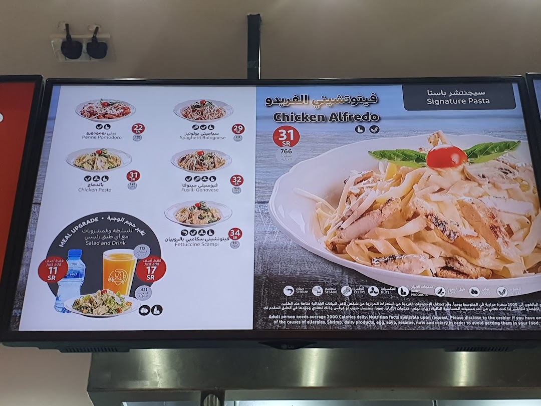 A digital menu board displaying various pasta dishes and a meal upgrade option.