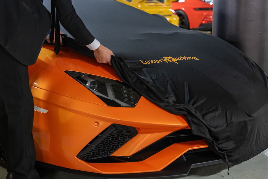 A person in a suit covers an orange sports car with a black car cover.