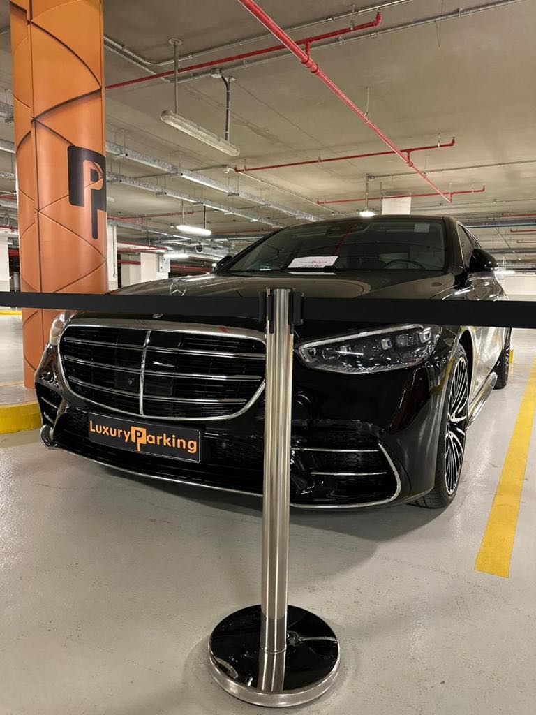 A black luxury car parked in a well-lit parking garage with "Luxury Parking" signage.