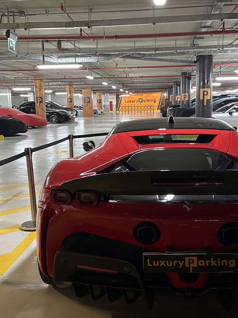 A red luxury sports car parked in a well-lit, modern parking garage with other vehicles.