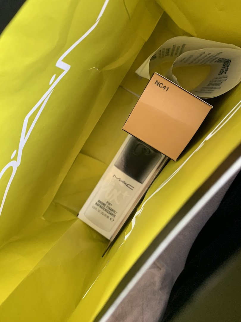 A M.A.C makeup product inside a bright yellow shopping bag.