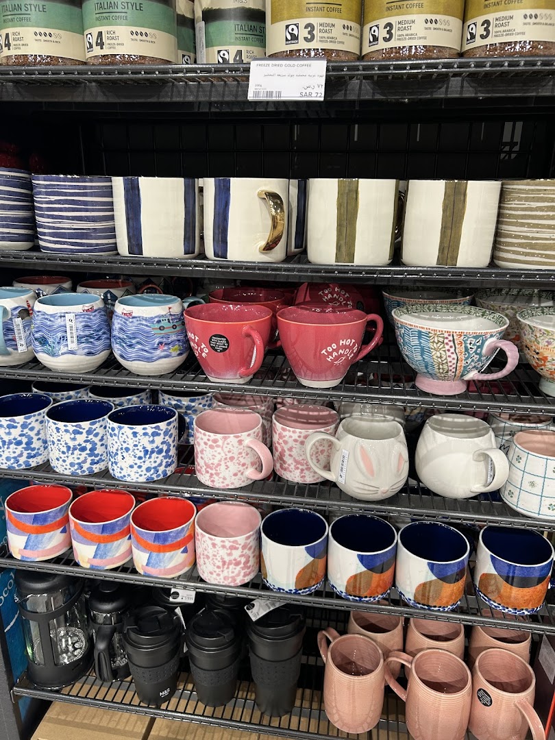 A display of various colorful mugs and coffee cups on shelves, with coffee products above.