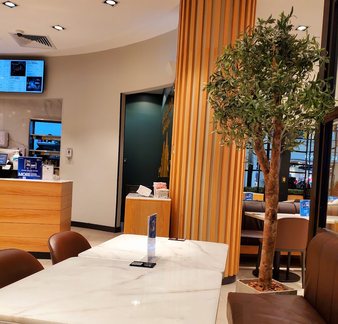 Interior of MS FOOD and MS CAFE with tables, chairs, a decorative tree, and a counter.
