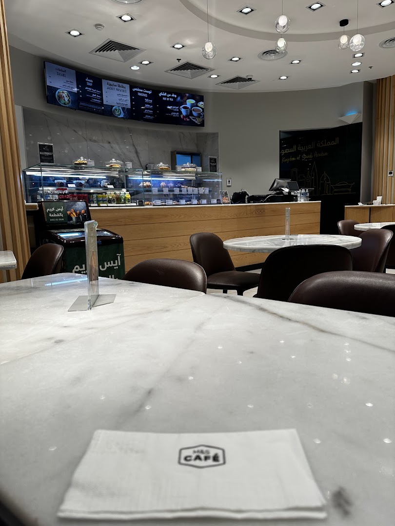 Interior of a cafe with a display counter, seating, and a menu board overhead.