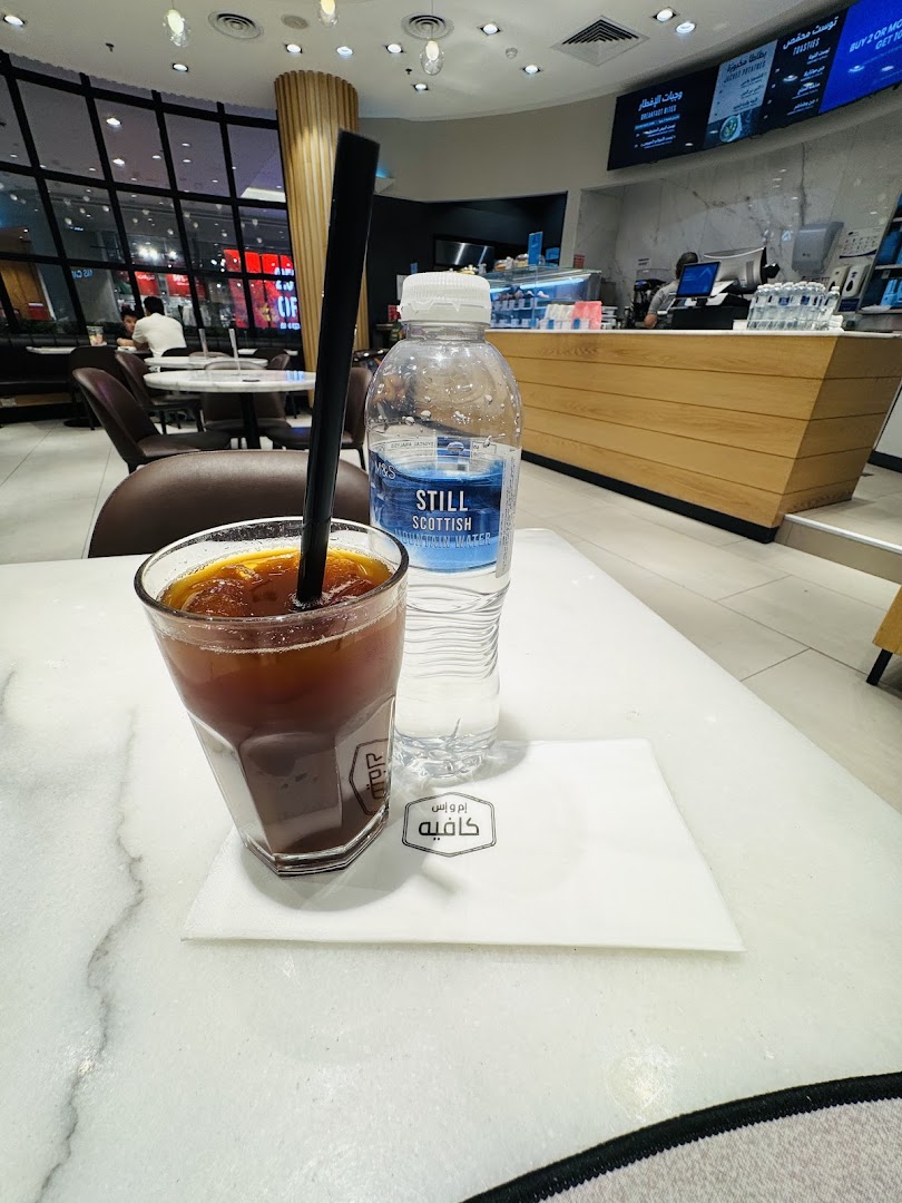A glass of iced coffee and a bottle of water on a table at MS FOOD and MS CAFE.