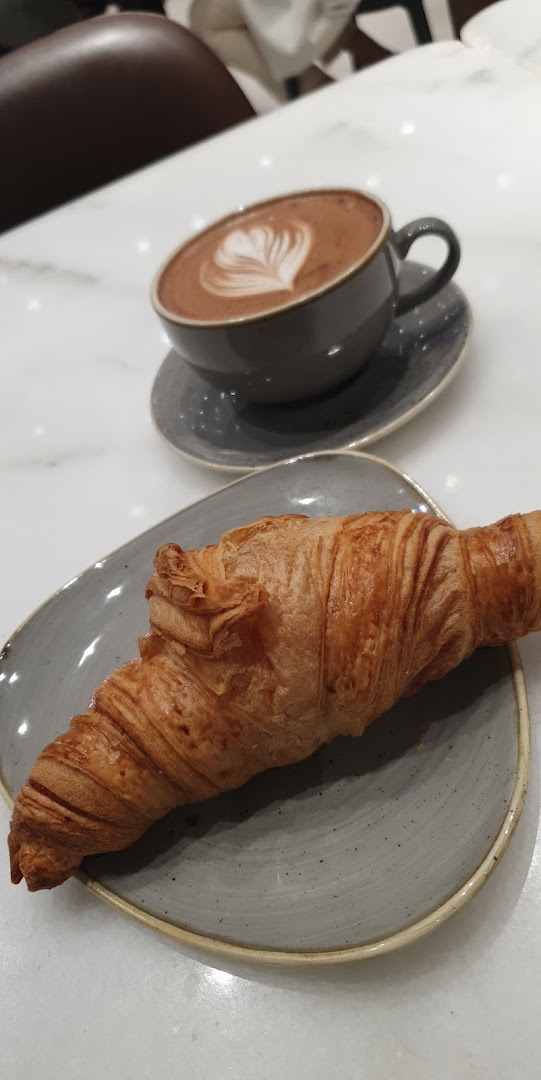 A delicious croissant and a cup of coffee with latte art on a marble table.