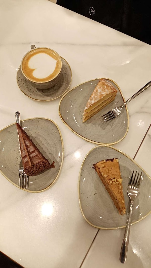 A coffee with latte art and three slices of cake on plates with forks.