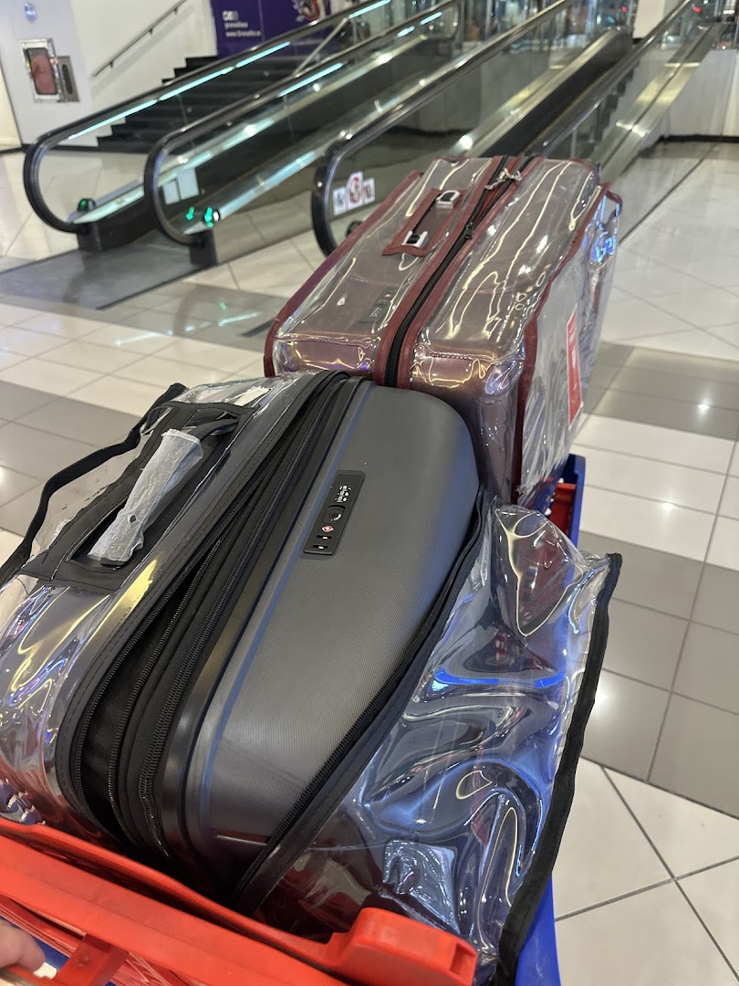 Two suitcases covered in clear plastic on a luggage cart in front of escalators.