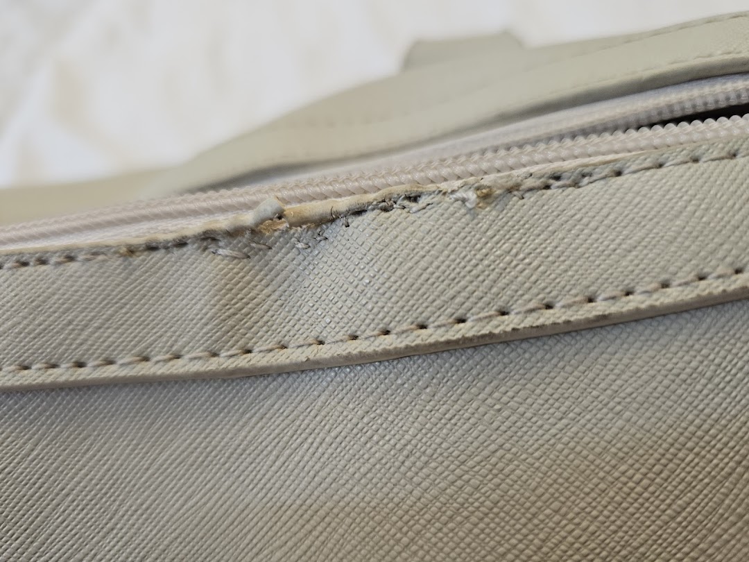 Close-up of a light-colored textured material with a zipper and stitching detail.