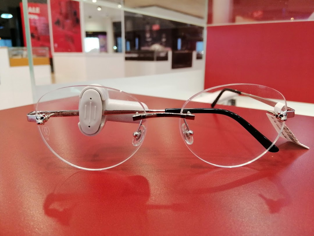 Close-up of rimless eyeglasses with a silver frame and black temples on a red surface.