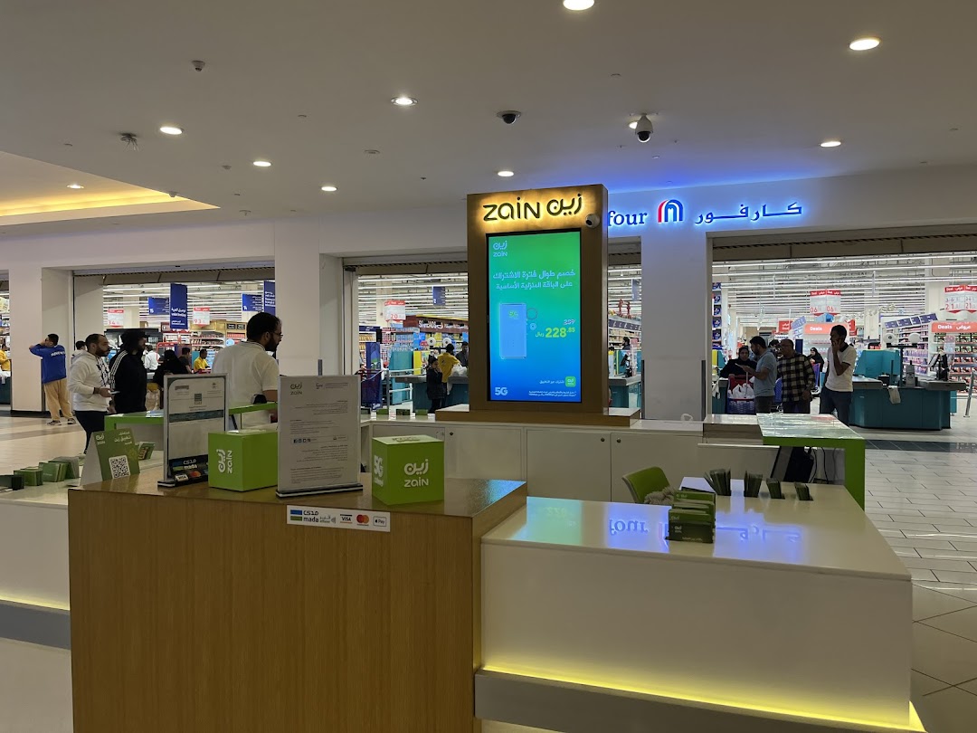 A Zain telecom kiosk with a digital display and customers in a shopping mall.