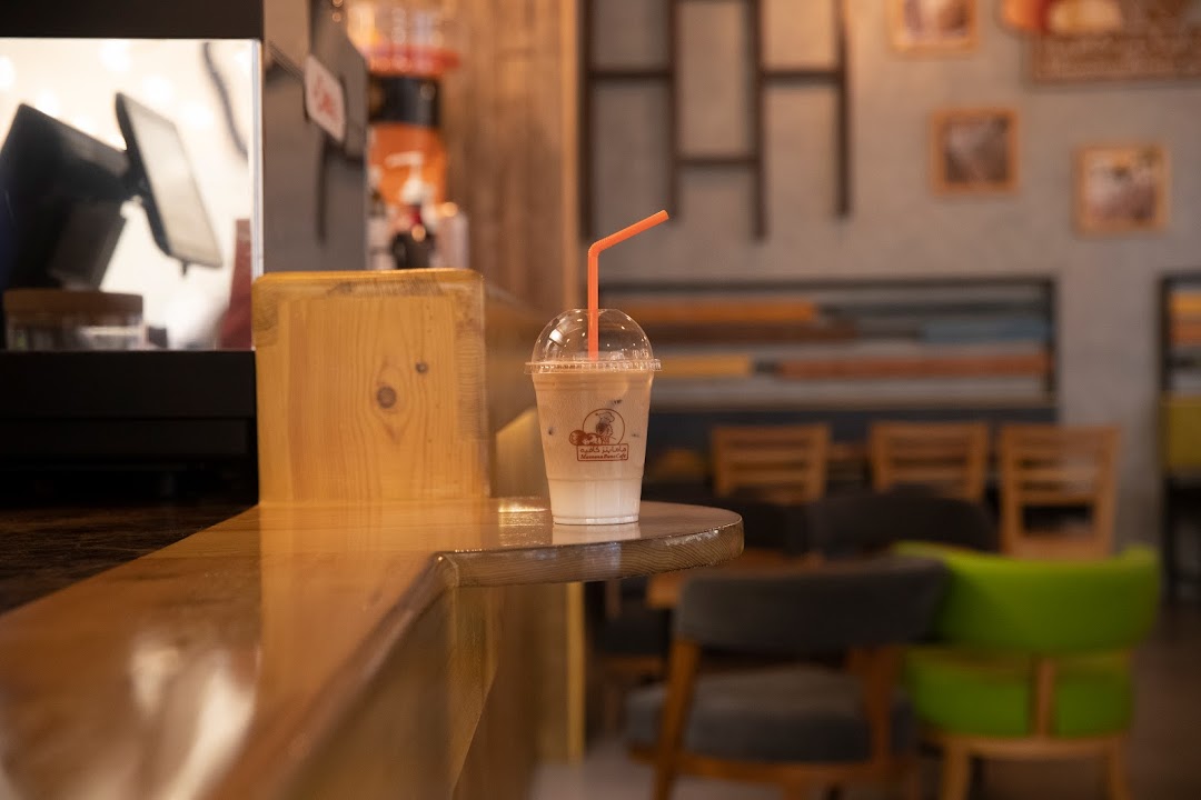 A refreshing iced coffee with a straw sits on a wooden counter in a cafe.