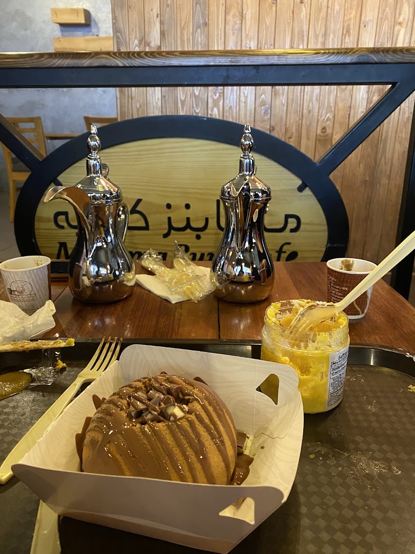 A delicious chocolate-covered bun with a side of yellow spread and traditional coffee pots.