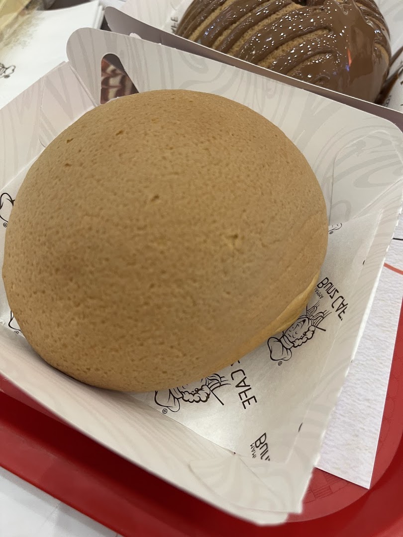 A close-up of a golden-brown bun served in a paper tray, with another pastry in the background.