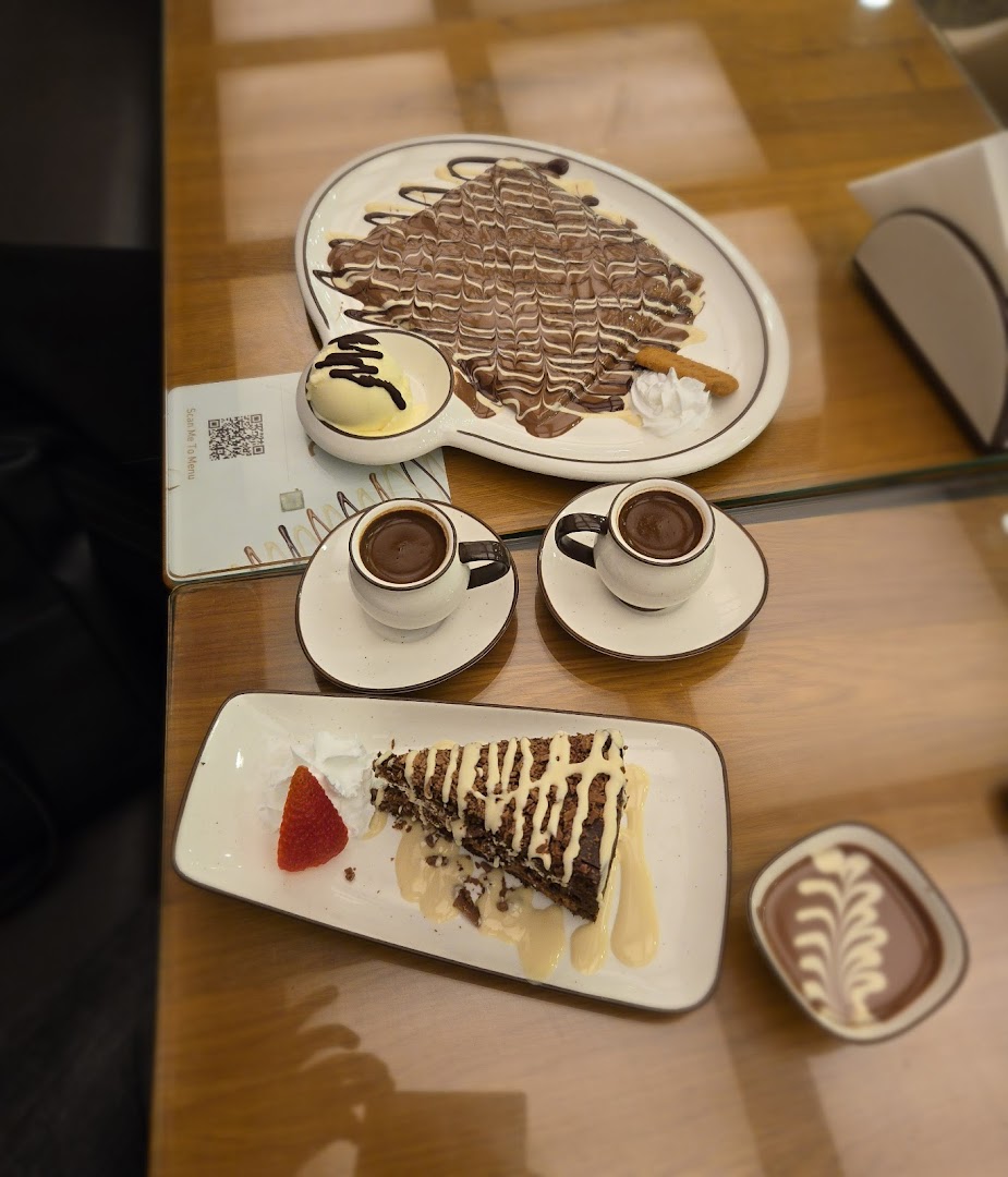 A table laden with delicious desserts and coffee, including a crepe, cake, and espresso cups.