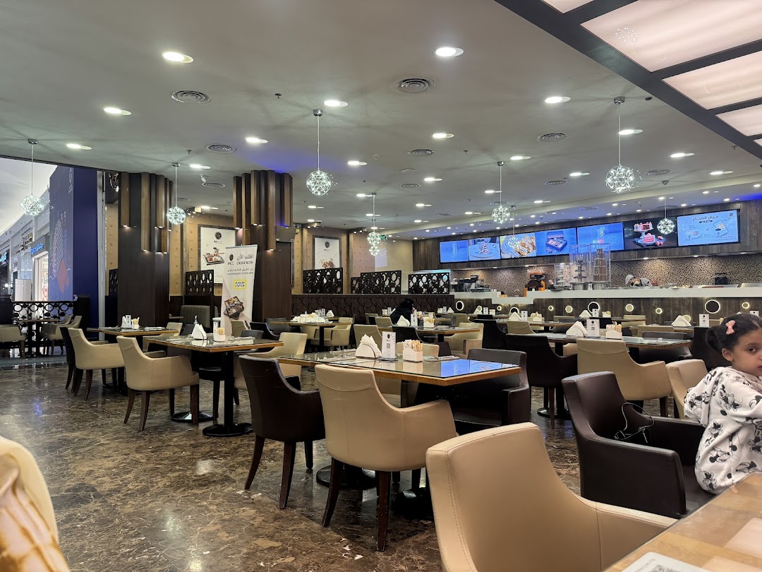 Interior view of a modern restaurant with tables, chairs, and digital menu screens.