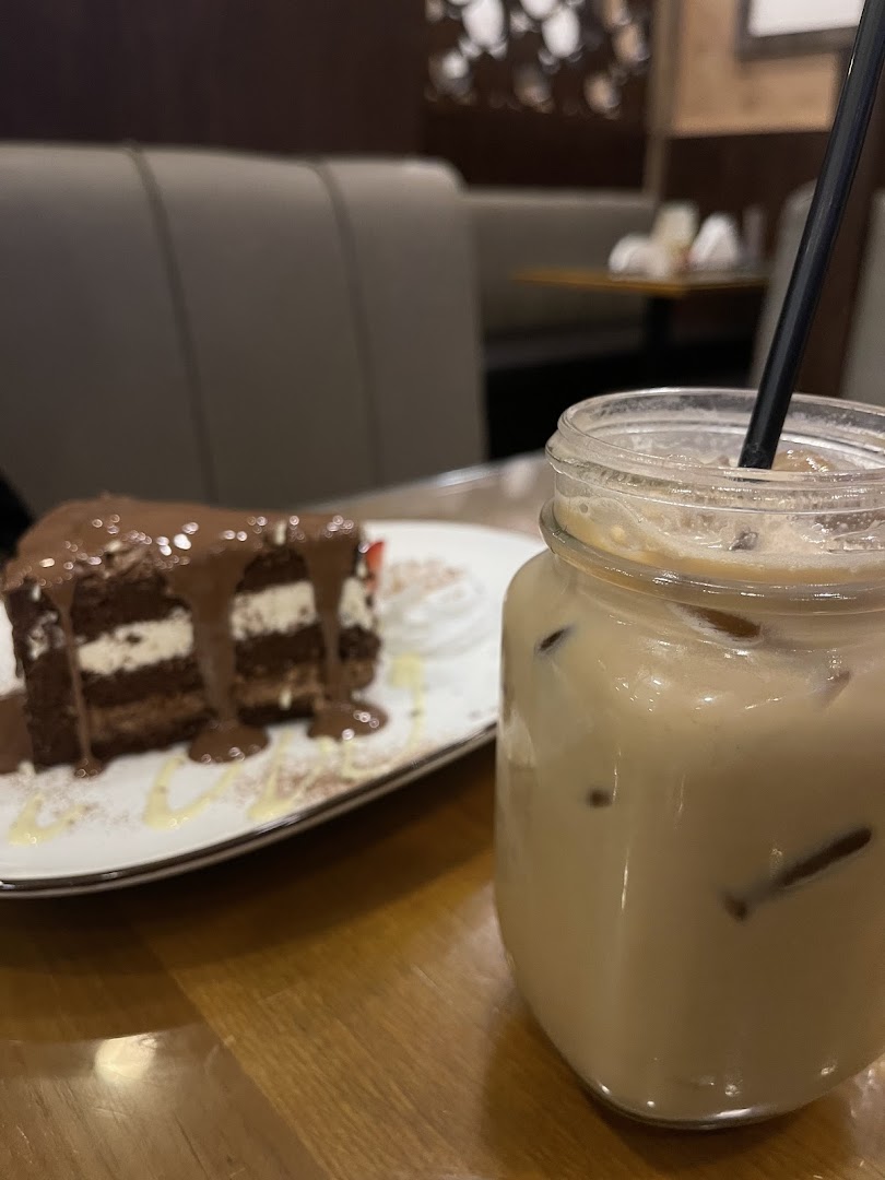 A slice of chocolate cake with whipped cream and a glass of iced coffee on a wooden table.