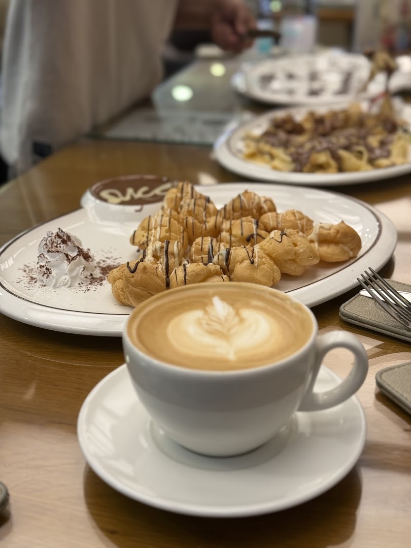 A cup of latte art coffee and a plate of cream puffs with chocolate sauce.