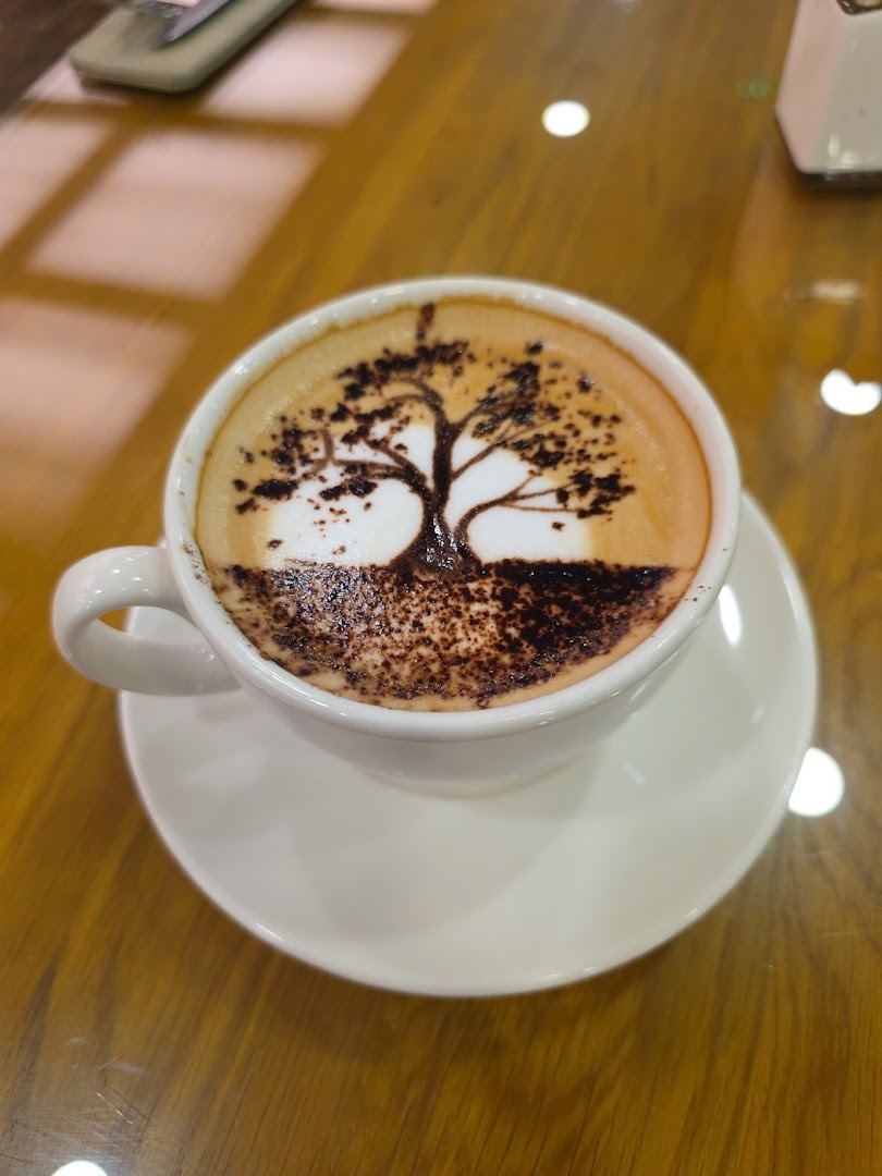 A close-up of a white cup of coffee with latte art depicting a tree.