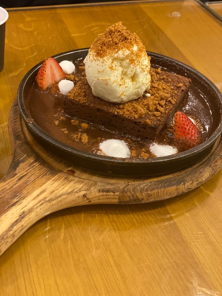 A warm brownie topped with ice cream, strawberries, and cookie crumbles served on a sizzling plate.