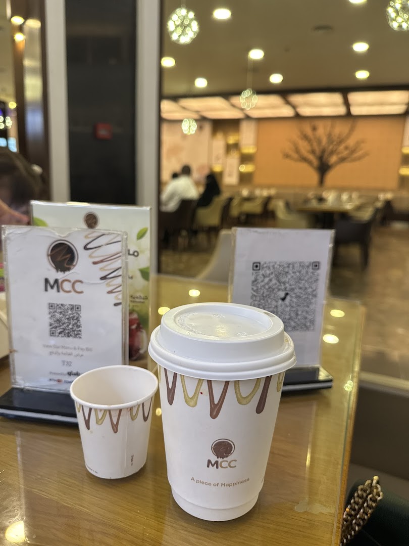A coffee cup and a small empty cup from MCC, with a QR code and menu stand on a table.