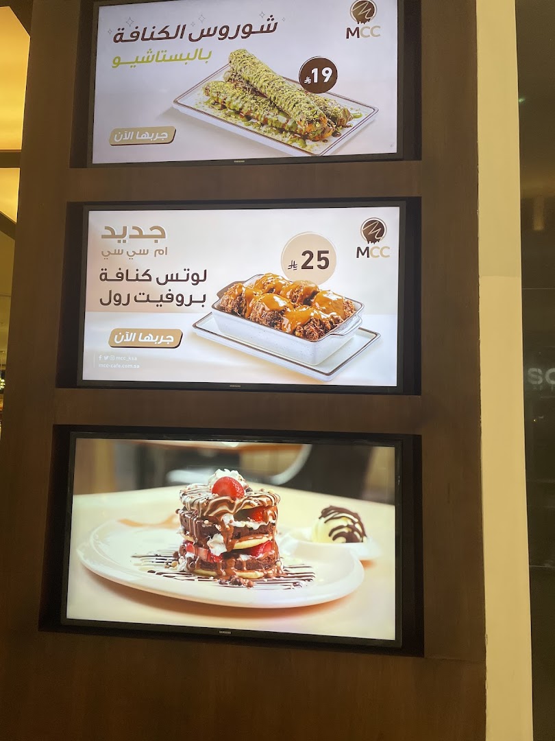 Three illuminated screens display tempting desserts from MCC, featuring pistachios, lotus, and chocolate.