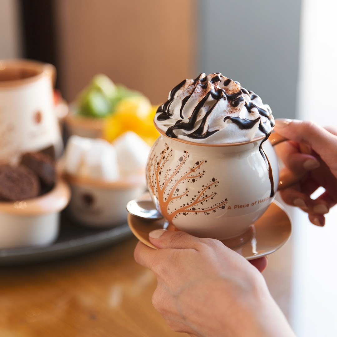 A person holds a decorative mug filled with whipped cream and chocolate sauce.