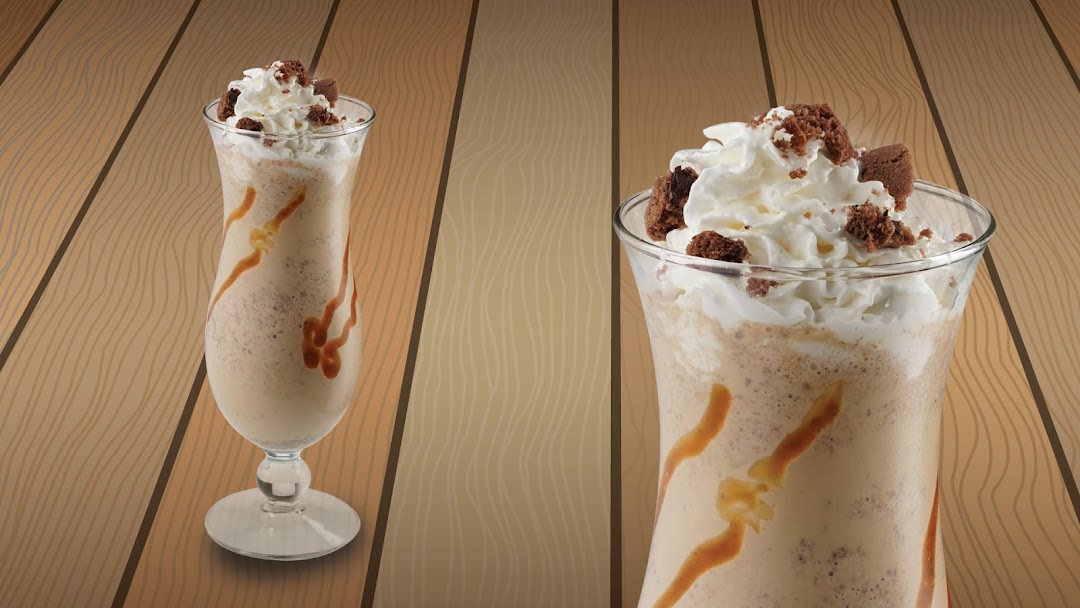Two delicious-looking milkshakes with whipped cream and brownie bits on a wooden background.