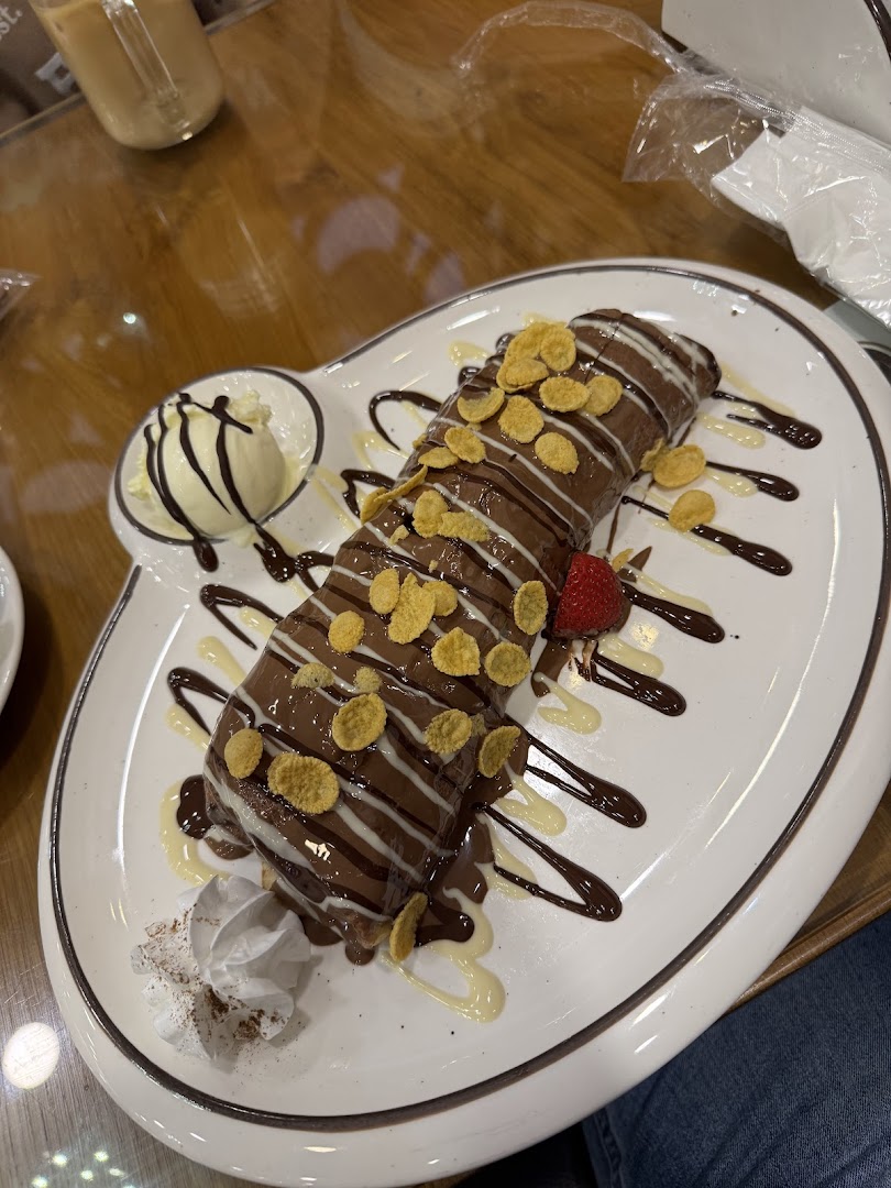 A delicious chocolate crepe topped with cereal, drizzled with sauces, and served with ice cream.