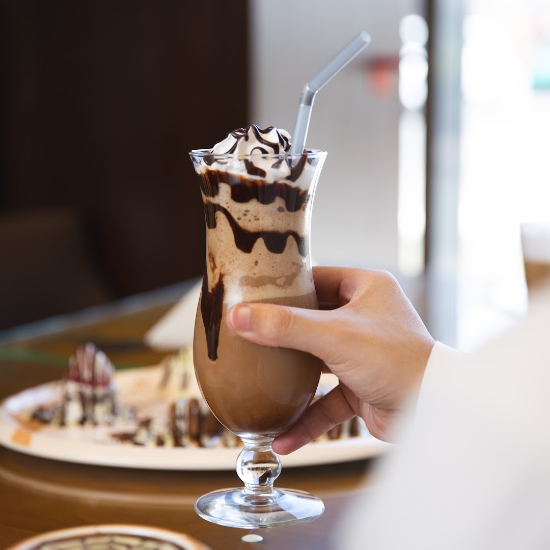 A hand holds a decadent chocolate milkshake topped with whipped cream and chocolate syrup.